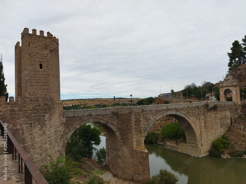 Fototapeta premium Puente de piedra medieval con torre defensiva sobre un río bajo un cielo nublado