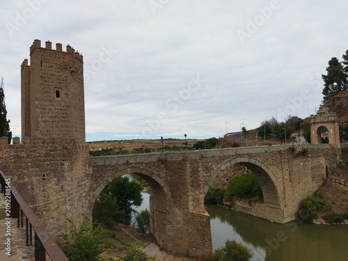 Puente de piedra medieval con torre defensiva sobre un río bajo un cielo nublado
