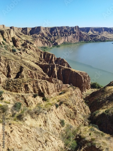 Impresionante cañón de arcilla con acantilados erosionados junto a un río bajo un cielo azul