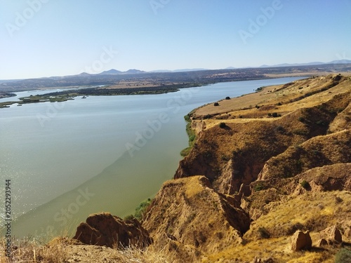 Vista panorámica de acantilados de arcilla junto a un gran embalse de agua bajo un cielo azul despejado