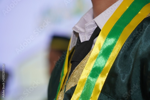 Foto Close-up of a student wearing a green graduation gown with a yellow and green sash during a commencement ceremony, representing education, achievement, and academic success