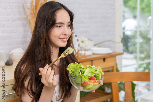 Happy with Salad:Delicious and Healthy:Image of a girl holding a bowl of colorful fresh salad,smiling happily.Natural light shining into the kitchen conveys happiness with eating nutritious food.