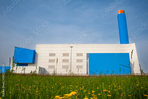 Valokuva Struttura industriale moderna con pannelli blu, camino cilindrico e prato fiorito in primo piano