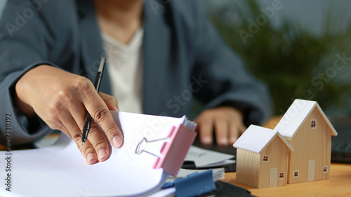 Fotografie Real estate agent reviewing property documents and mortgage paperwork with model houses on office desk