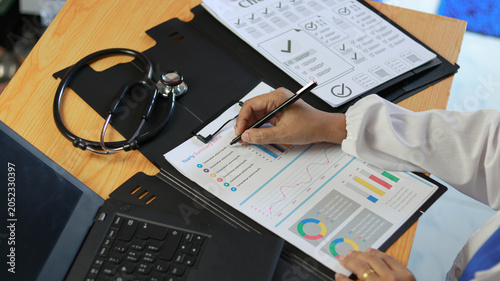 Photos Healthcare professional analyzing medical reports and performance data on office desk with stethoscope and laptop