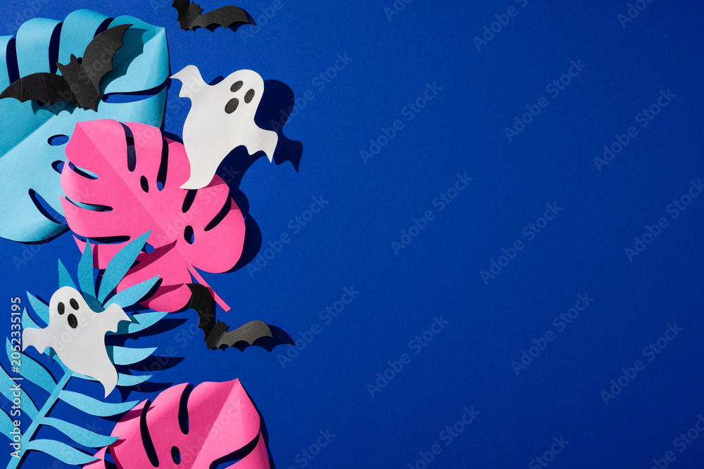 Naklejka premium Tropical Halloween paper ghosts bats and bright monstera leaves on blue background for party decor