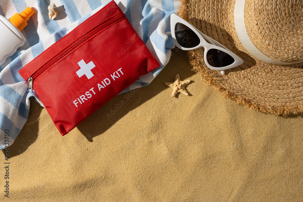 Naklejka premium First aid kit and sun protection essentials on a sandy beach towel for safe summer travel