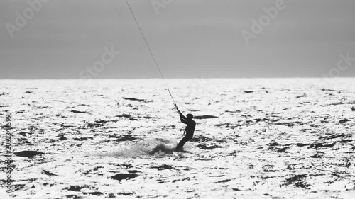 Kitesurfer rides waves in coastal waters during overcast afternoon