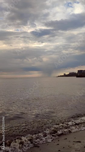 Rainy weather at sea near urban coast. Dark cloudy rainy clouds in sky, blue calm water surface of sea waves. Rain falling in sea. Seascape. Sea landscape. Nature backdrop Natural background Vertical