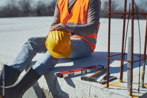 Foto Construction worker working outdoors on a construction site, making a pause and holding a yellow hardhat