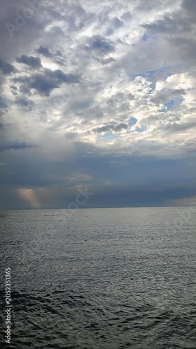 Rain in sea. Rain falling in sea. Cloudy, rainy, stormy weather at sea. Dark rainy clouds over water. Sea, sky, clouds and horizon line. Seascape. Scenery landscape. Nature natural background Vertical