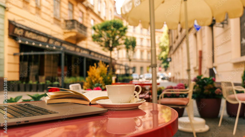 Fototapeta premium Enjoying a coffee break with a book and laptop at an outdoor cafe table