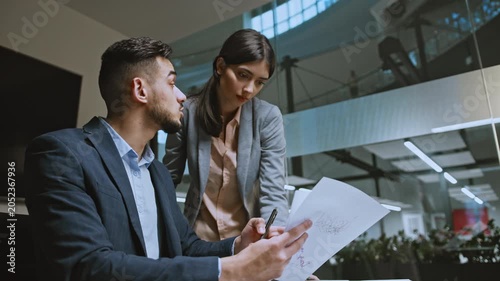Focused Asian Male And Female Professionals Reviewing Important Documents Together At Modern Office Workspace. Engaged In Discussion About Project Requirements And Business Strategies, Collaboration.