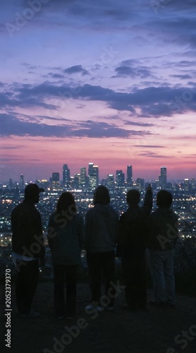 Group of friends silhouetted against a city skyline at dusk watching the glowing skyscraper lights from a hill viewpoint at twilight