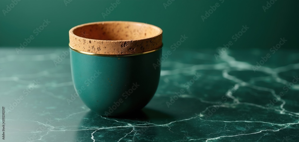 Fototapeta premium Teal cup with cork rim and gold accent sits on dark green marble surface. Smooth background is a deep teal shade. Minimalist elegant drinkware.