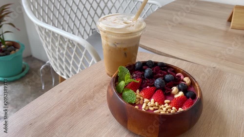 Healthy berry smoothie bowl with strawberries, blueberries, dried berries, nuts and fresh mint, served alongside iced coffee in a cozy modern café. Nutritious breakfast and wellness lifestyle concept