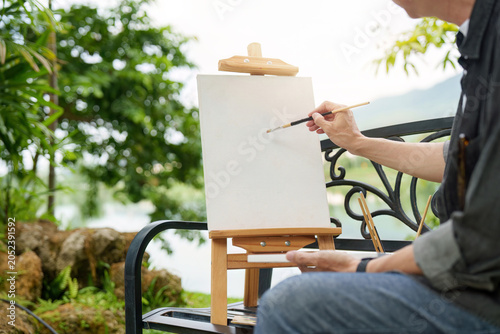 Bild auf Leinwand Man painting on easel outdoors in a lush garden for creative hobby