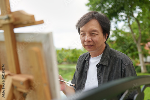 Foto Asian senior man painting on easel outdoors in a lush garden for creative hobby