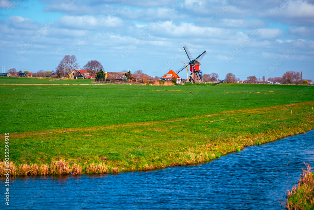 Fototapeta premium Vibrant green pasture and blue canal leading towards a traditional Dutch windmill in the countryside
