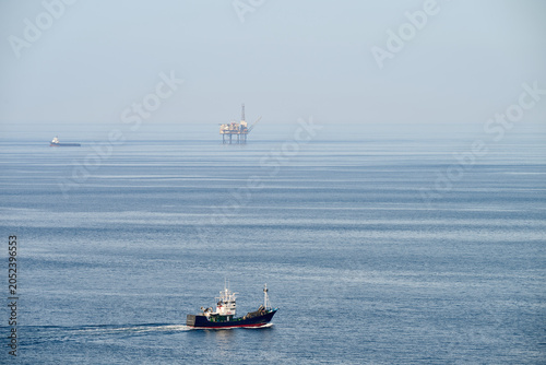 Fishing boat transiting blue ocean near oil platform