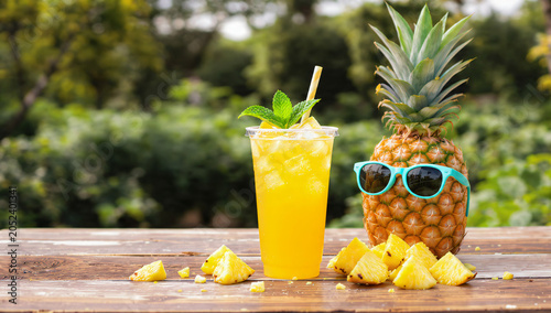 Refreshing Pineapple Juice in a Clear Cup Beside a Cool Pineapple Wearing Sunglasses on a Wooden Table