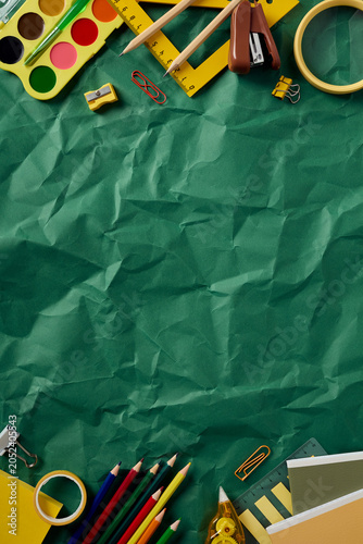 Vertical flat lay of back to school supplies. Top and bottom borders on a green crumpled paper