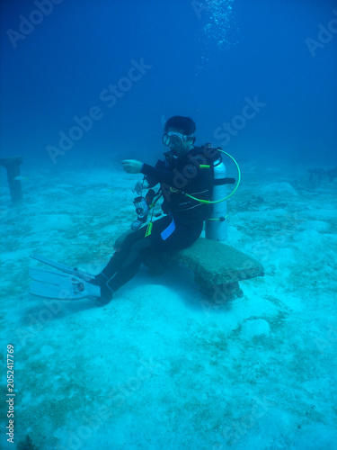 Scuba diver sitting on a stone bench underwater on a sandy tropical seabed
