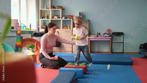 Woman helps a young boy navigate colorful blocks in a vibrant children's playroom, surrounded by various toys and educational items