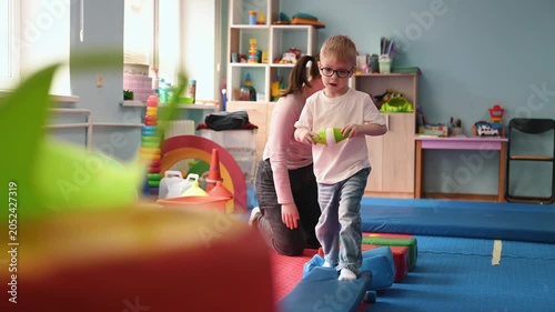 Woman helps a young boy navigate colorful blocks in a vibrant children's playroom, surrounded by various toys and educational items