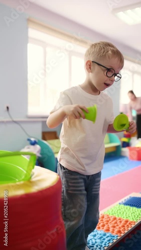 Woman helps a young boy maintain balance on foam blocks in a vibrant playroom, surrounded by various educational toys and colorful mats