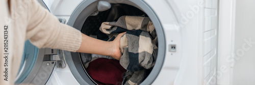 Laundry washing machine clothing hand home appliance clean fabric loading clothes into front load washer in bright utility room for household chore