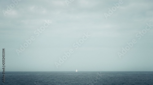 Small sailboat on the open ocean under a cloudy sky