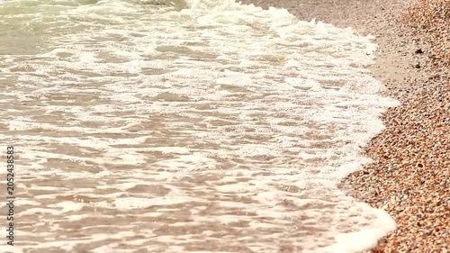 Small sea waves approaching shore, sand and water in closeup, foamy waves washing onto beach, calm coastal environment, natural seaside scene with relaxing atmosphere