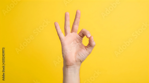 Hand making ok gesture on yellow background