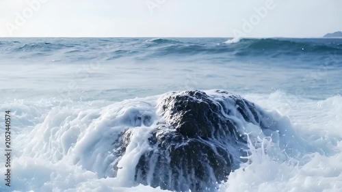 Blue ocean wave crash over rock shore, sea spray and white foam, coastal surf scene with calm mood, wet rock underwater