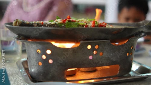 4K Close-up Thai steamed fish with chili and garlic on hot fish-shaped stove boiling with steam, Spicy local food traditional culinary.