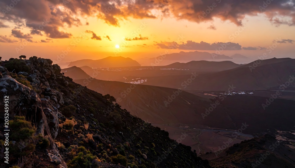 Obraz premium Stunning panoramic view of a mountain range at sunset with golden light, fluffy clouds, and a distant town