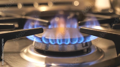 Medium close up of electric blue gas burner flame flickering on brushed steel stovetop