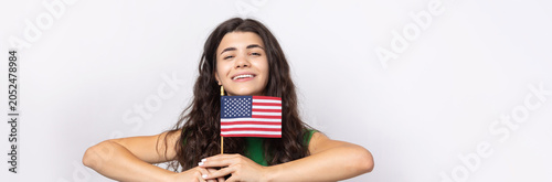 A young happy girl with a smile on her face holds an American flag in her hands. Symbol of patriotism and freedom.