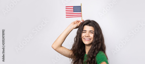 A young happy girl with a smile on her face holds an American flag in her hands. Symbol of patriotism and freedom.