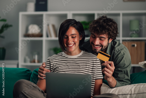 Fotografie Happy couple shopping online together from home using laptop and credit card for