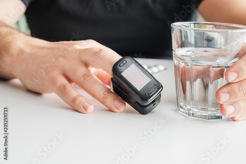 Foto Mature man checks his blood oxygen with a fingertip pulse oximeter beside a glass of water illustrating home health monitoring vitals checking and preventive self care