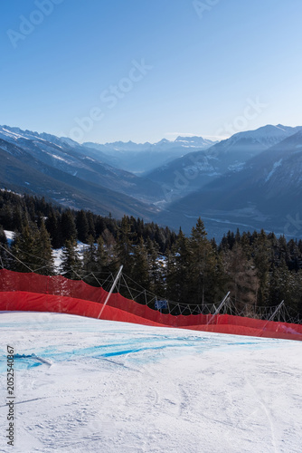 Type A safety structure with red protection net and OB pole at racecourse of the Alpine Ski World Cup in Crans-Montana, Switzerland with senic view over Rhone Valley