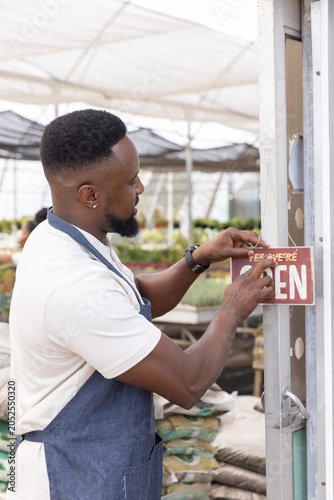 Red OPEN sign is being attached to metal door frame at nursery entrance, with potted plants