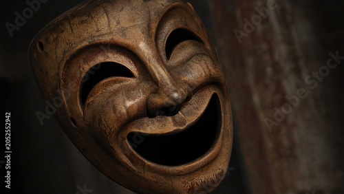 Vintage wooden theater mask with exaggerated smile, dramatic side lighting on textured surface.