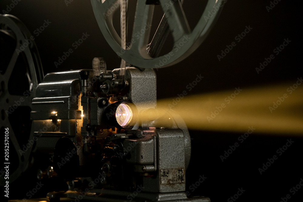 Fototapeta premium Old film projector shows light beam in dark room during movie screening