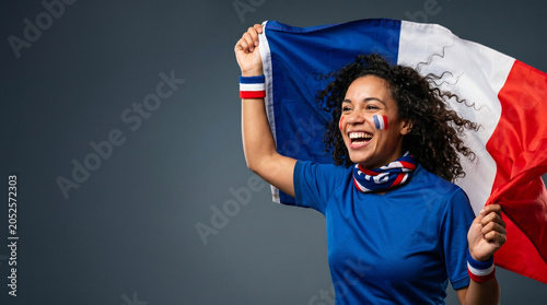 Joyful female football fan holding French flag, celebrating victory, smiling woman supporter in blue shirt with face paint cheering for France national team, isolated on gray background