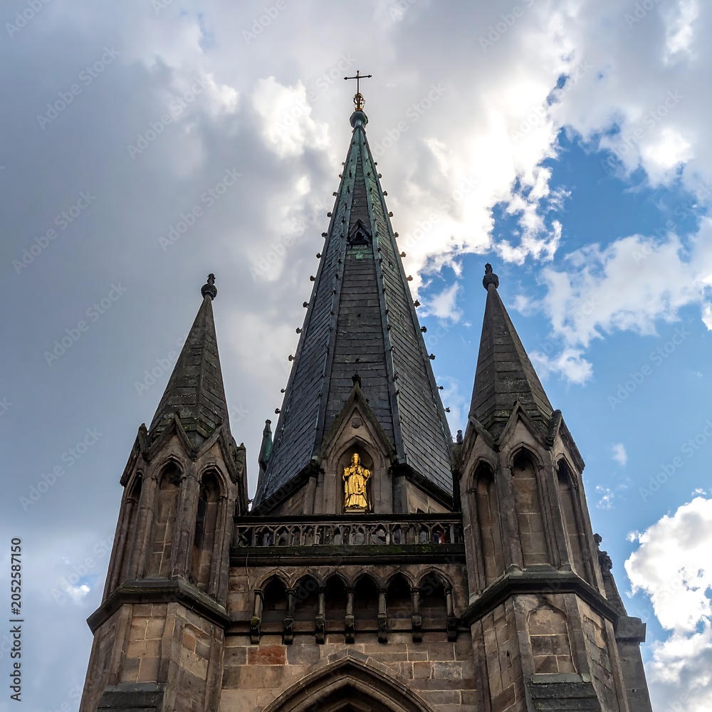 Fototapeta premium A Gothic-style church tower with a tall, pointed spire and two shorter spires on either side