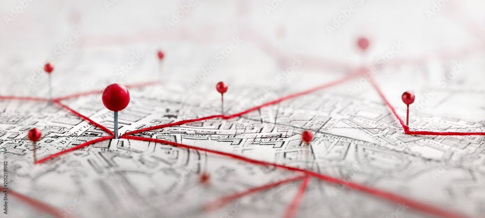 Obraz premium Close-up of a city map with red push pins connected by red thread, illustrating a network of locations, routes, logistics, planning, navigation, travel, business connections, geographic data