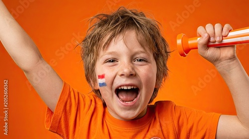 Excited young child with Dutch flag face paint and vuvuzela cheers for sports event
